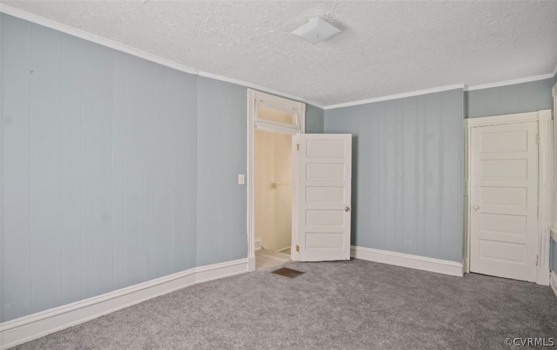 Unfurnished bedroom with ornamental molding, dark carpet, and a textured ceiling