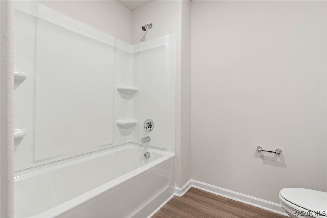 Bathroom with shower / bathing tub combination, hardwood / wood-style floors, and toilet