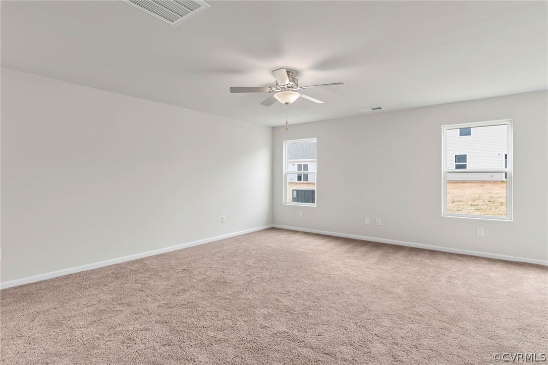 Carpeted spare room featuring ceiling fan and a wealth of natural light