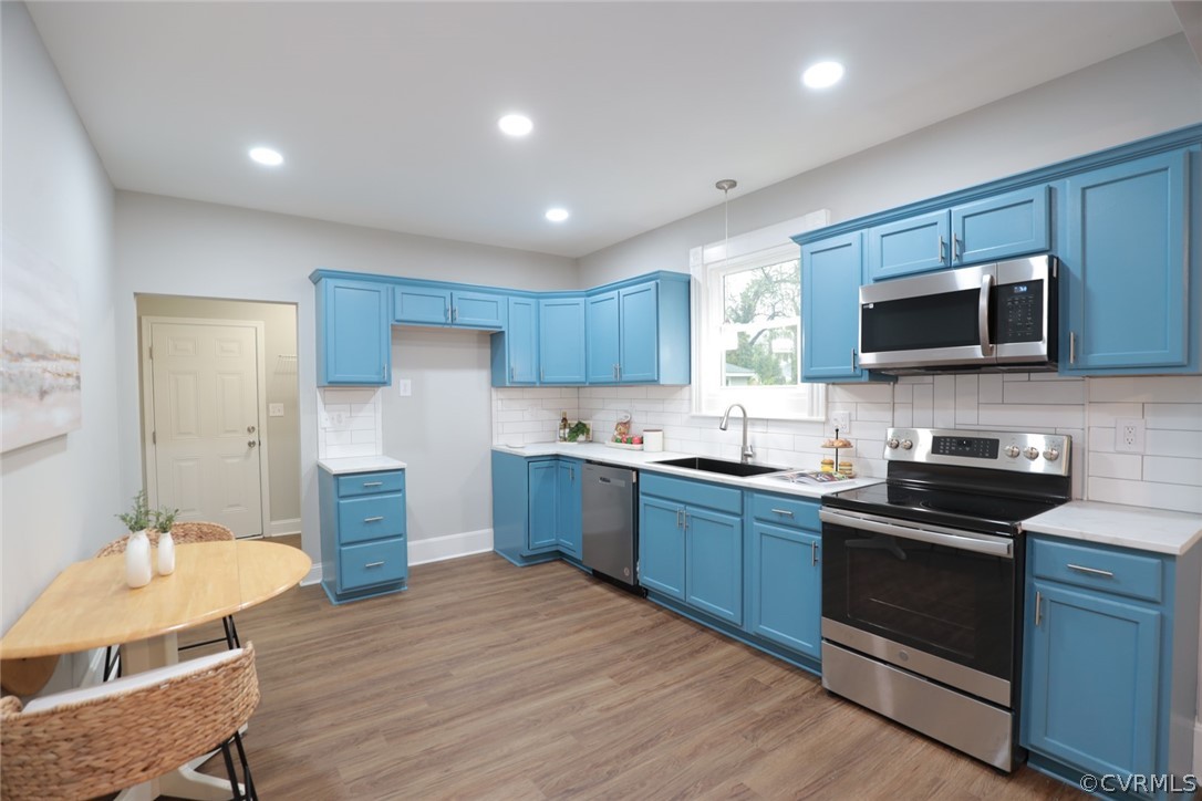 Kitchen with hardwood / wood-style floors, appliances with stainless steel finishes, sink, blue cabinetry, and tasteful backsplash