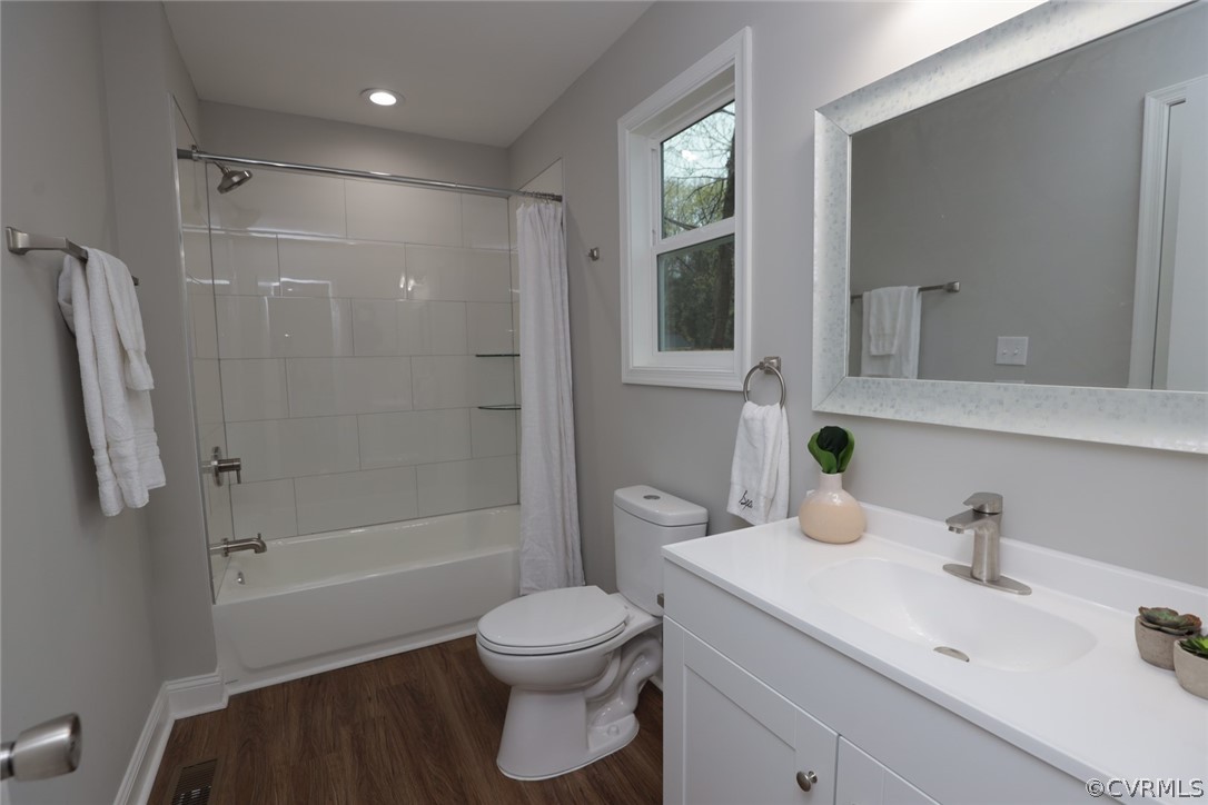 Full bathroom featuring large vanity, wood-type flooring, toilet, and shower / bathtub combination with curtain