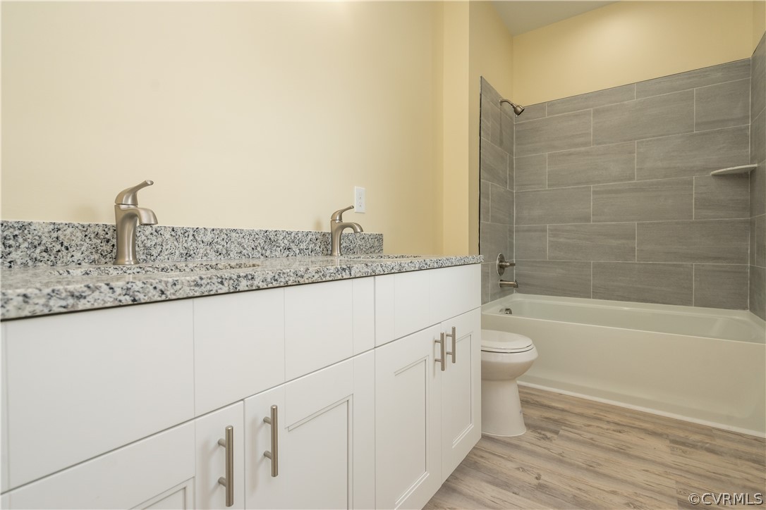 Full bathroom with vanity, tiled shower / bath combo, toilet, and hardwood / wood-style flooring
