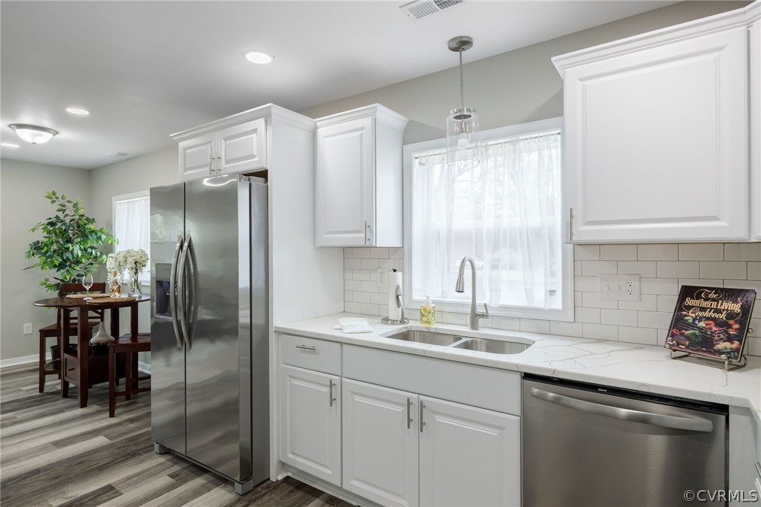 Kitchen with stainless steel appliances, hardwood / wood-style flooring, white cabinetry, backsplash, and sink