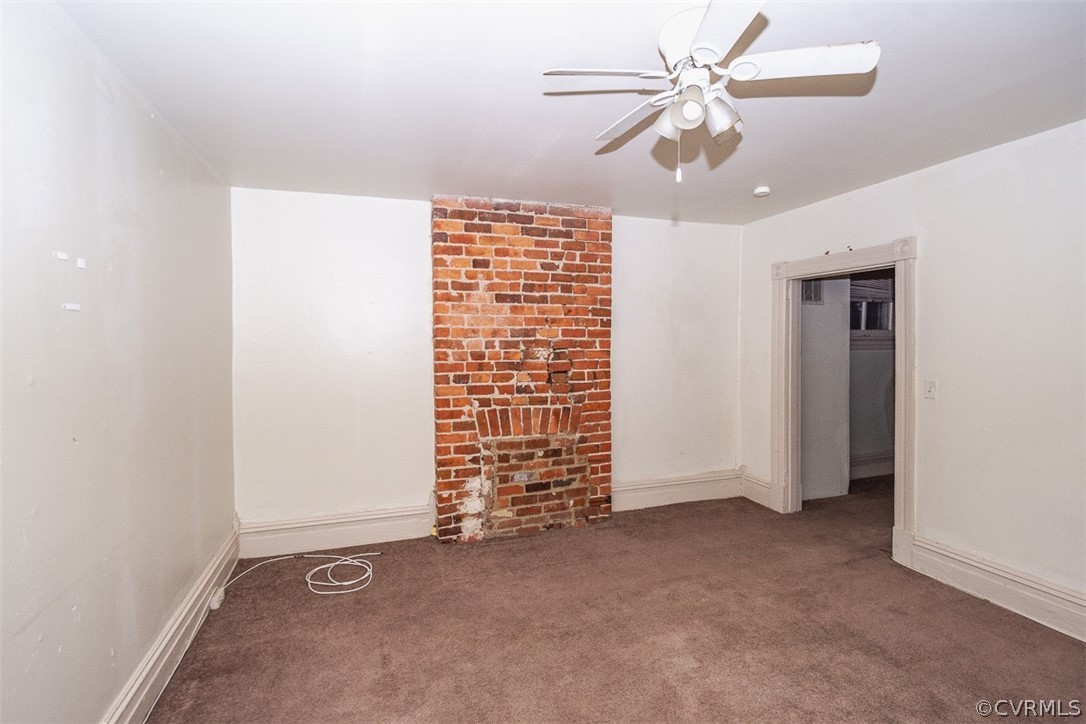 Spare room featuring brick wall, ceiling fan, and dark carpet