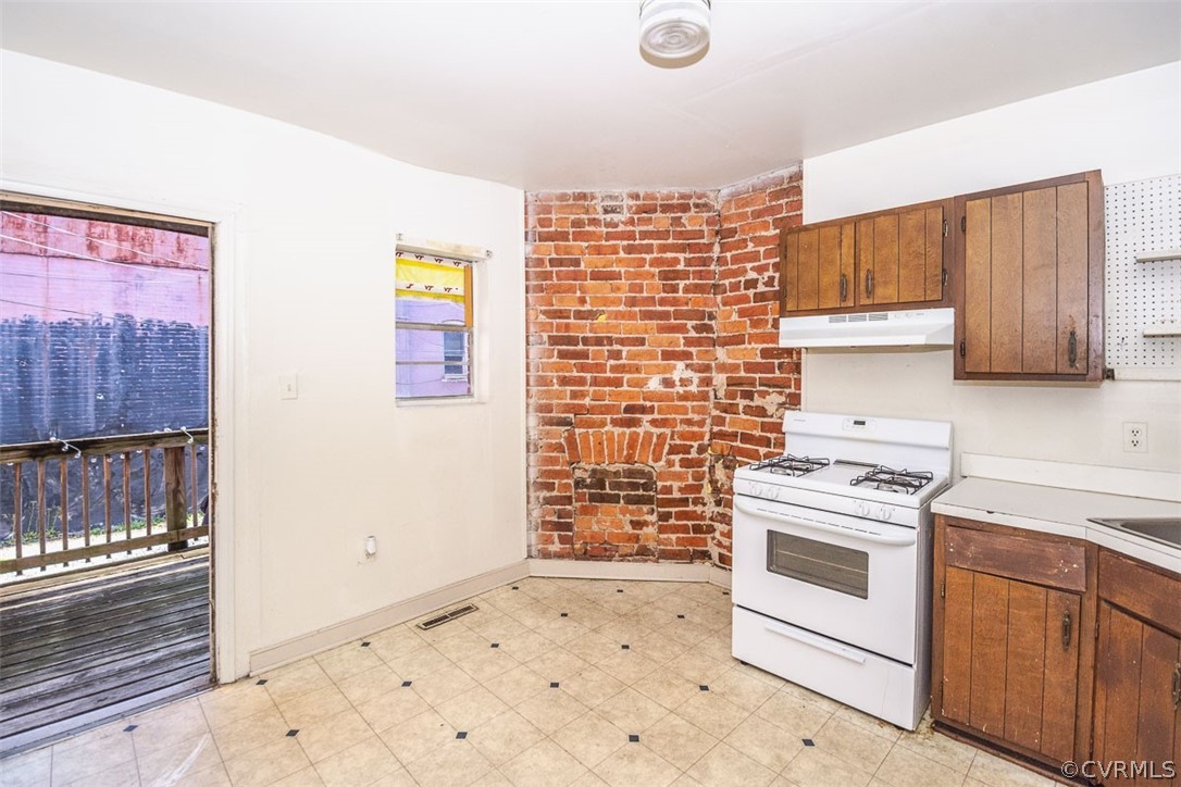 Kitchen featuring light tile floors, white gas range oven, and brick wall