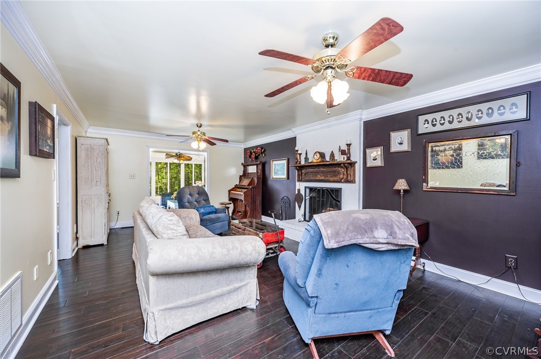 Living room with ceiling fan, dark wood-type flooring, and ornamental molding