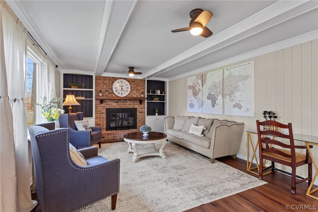 Living room featuring beamed ceiling, ceiling fan, built in shelves, and a brick fireplace
