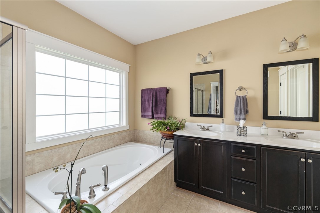 Bathroom featuring a relaxing tiled bath, double sink, vanity with extensive cabinet space, and tile flooring