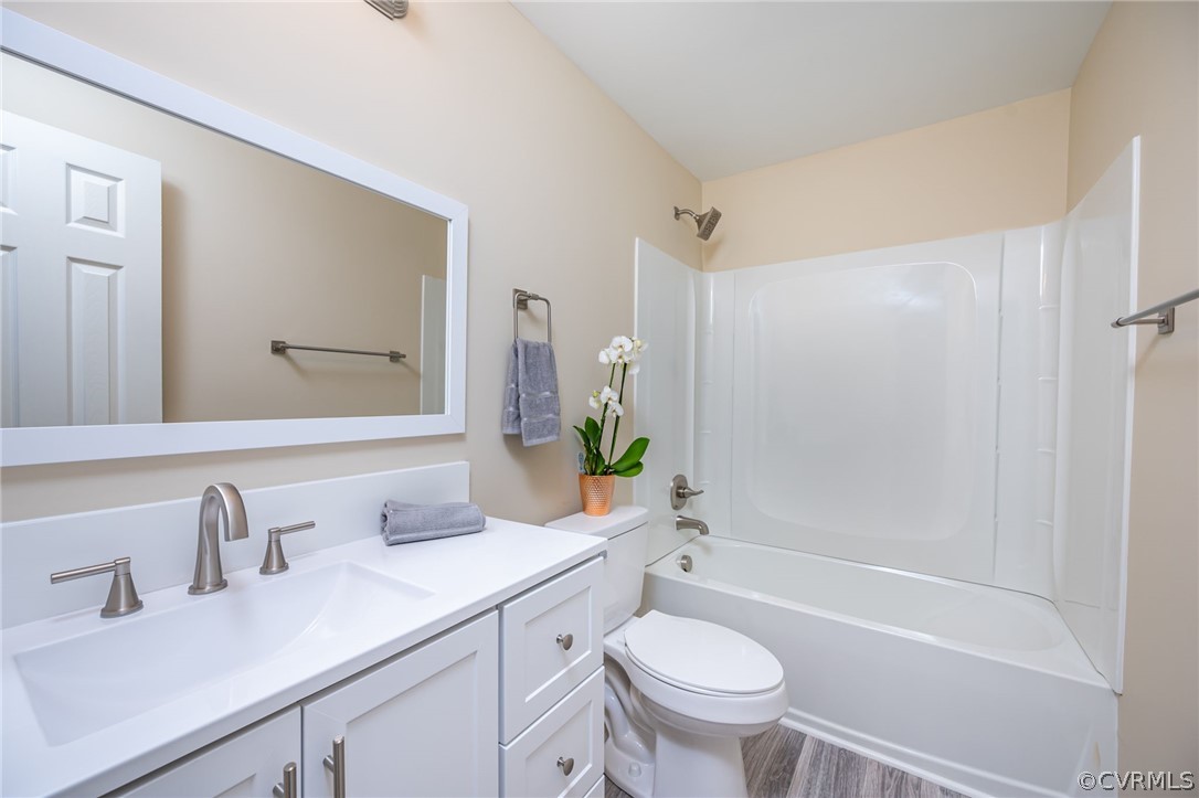 Full bathroom featuring toilet, large vanity, shower / bathing tub combination, and wood-type flooring