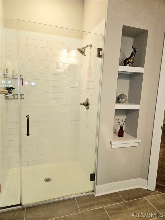 Bathroom featuring built in shelves, a shower with door, and tile flooring