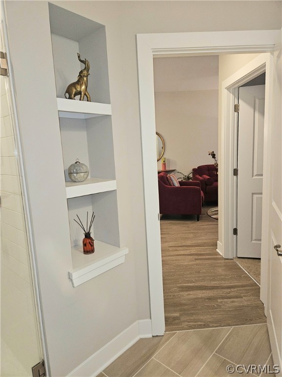 Hallway with light hardwood / wood-style floors and built in shelves
