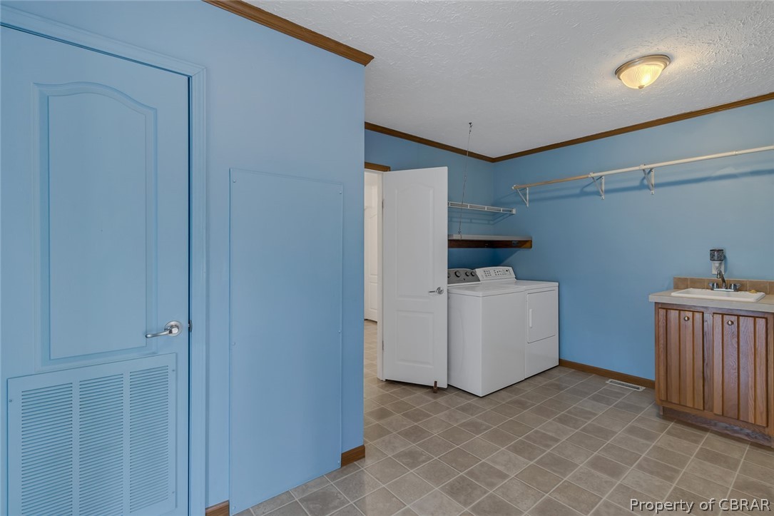 Laundry room featuring independent washer and dryer, sink, light tile floors, ornamental molding, and a textured ceiling