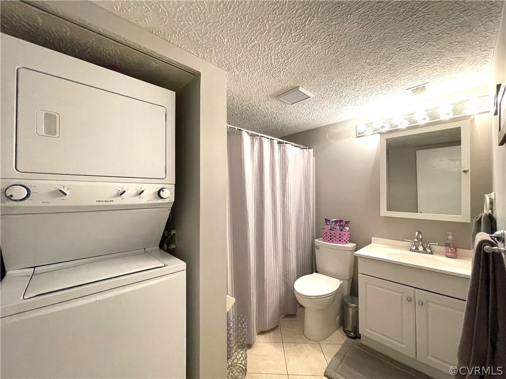 Washroom with a textured ceiling, stacked washing maching and dryer, sink, and light tile floors
