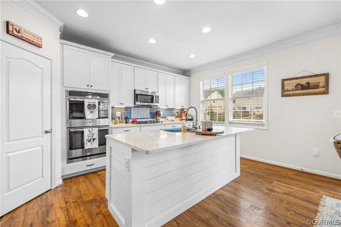 Kitchen featuring an island with sink, white cabinets, appliances with stainless steel finishes, and dark wood-type flooring