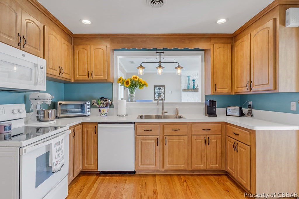 Kitchen featuring decorative light fixtures, light hardwood / wood-style floors, white appliances, and sink