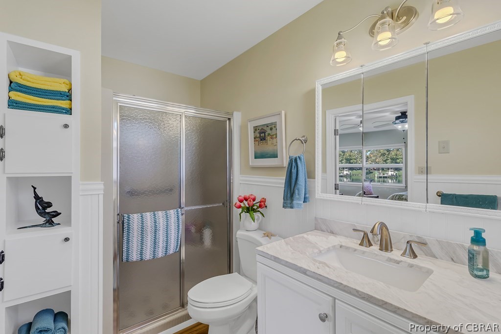 Bathroom featuring a shower with shower door, vanity with extensive cabinet space, ceiling fan, and toilet
