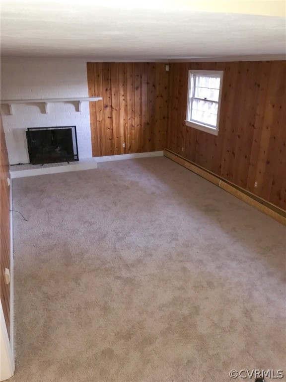 Unfurnished living room with wooden walls, a fireplace, a baseboard heating unit, and carpet
