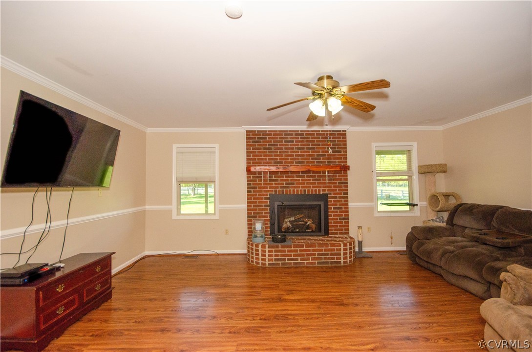 Living room with ceiling fan, a brick fireplace, hardwood / wood-style floors, brick wall, and ornamental molding