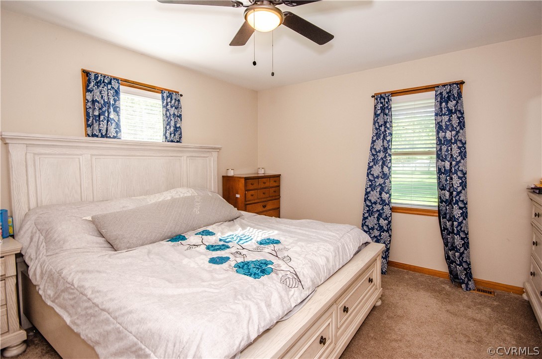 Bedroom featuring light carpet, ceiling fan, and multiple windows