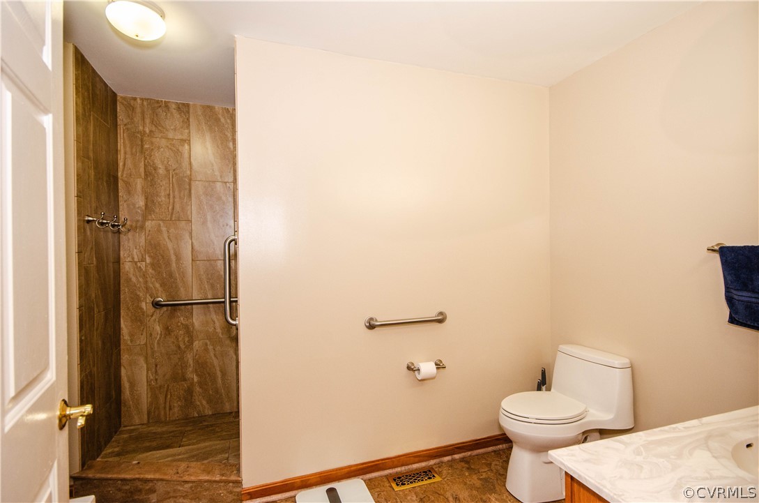 Bathroom featuring tiled shower, toilet, tile floors, and vanity