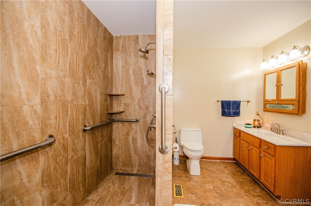 Bathroom featuring tile flooring, vanity, a tile shower, and toilet