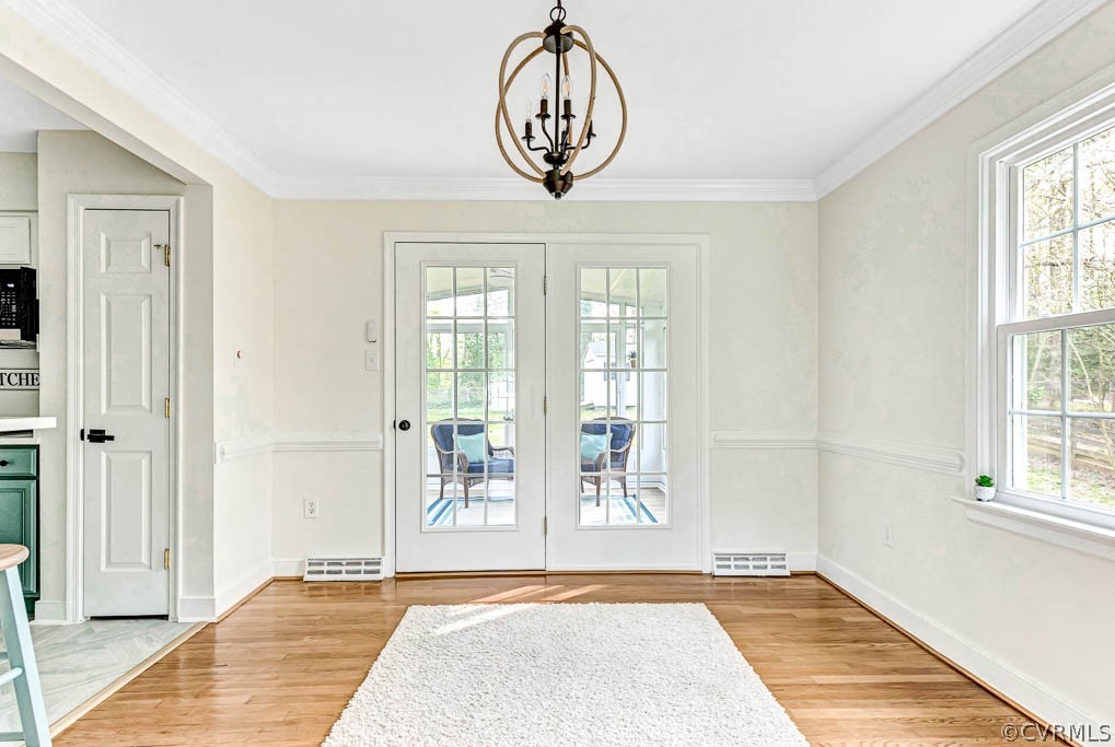 Doorway to outside featuring a notable chandelier, light wood-type flooring, french doors, and a healthy amount of sunlight