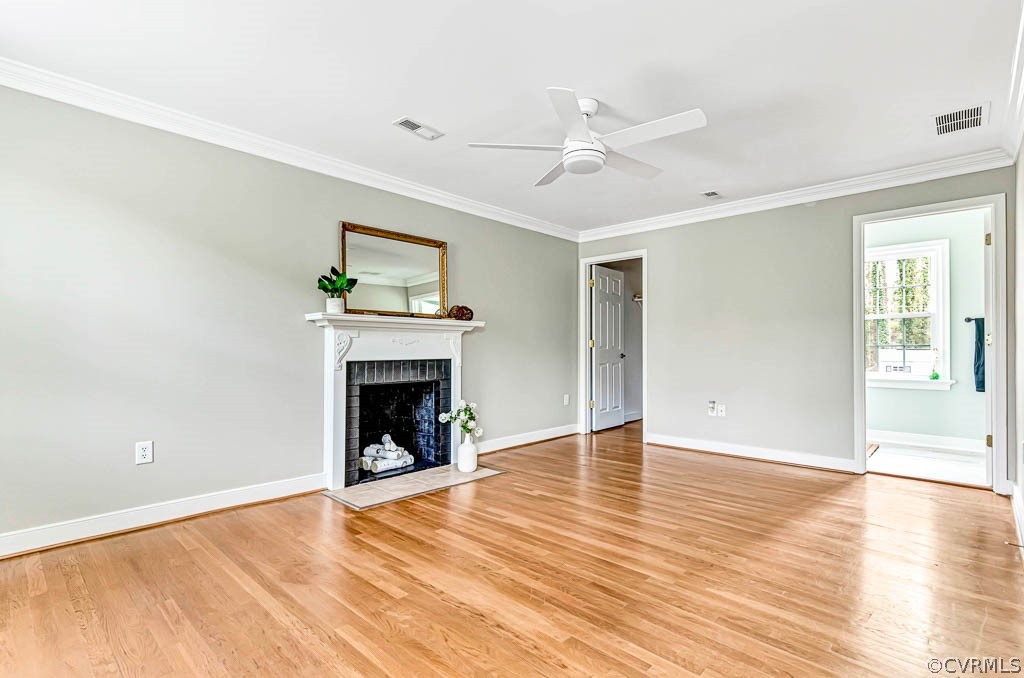 Unfurnished living room with ceiling fan, a brick fireplace, light hardwood / wood-style flooring, and crown molding