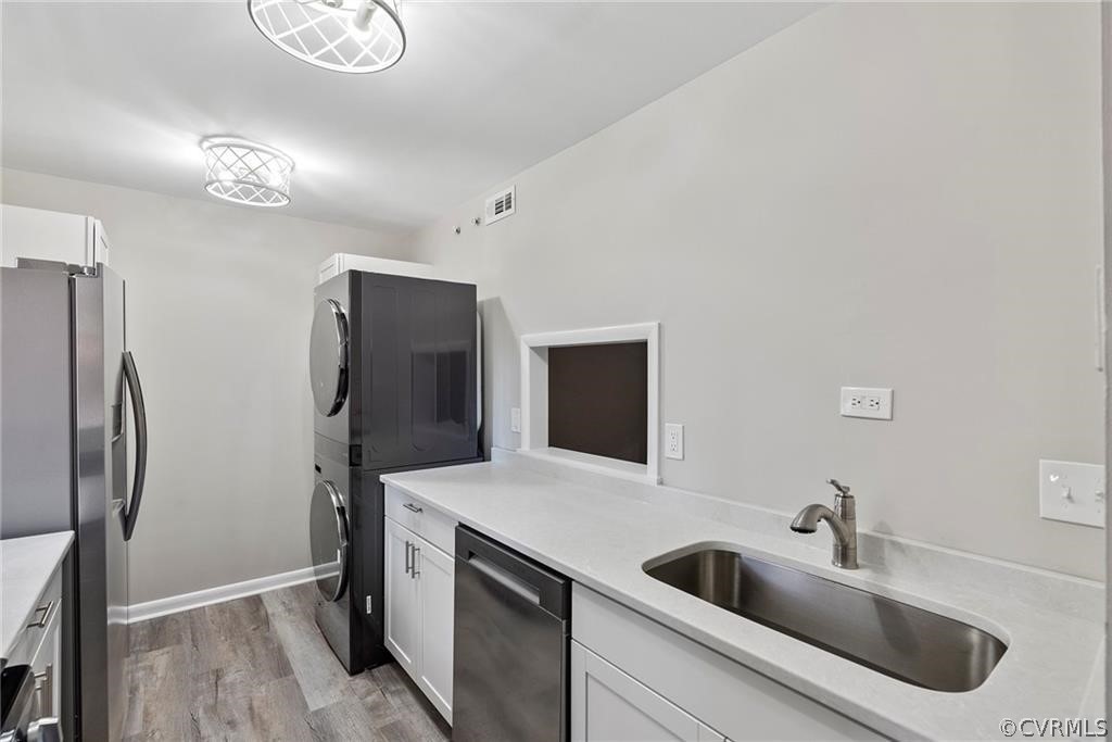 Kitchen featuring stacked washer / dryer, stainless steel fridge with ice dispenser, white cabinets, dishwasher, and light hardwood / wood-style​​‌​​​​‌​​‌‌​‌‌​​​‌‌​‌​‌​‌​​​‌​​ flooring