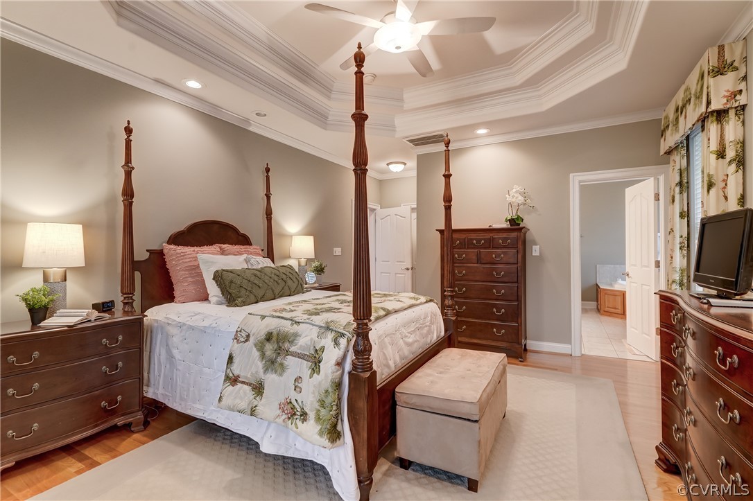 Bedroom featuring crown molding, connected bathroom, a tray ceiling, light tile floors, and ceiling fan