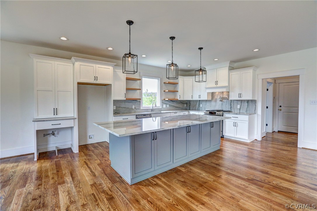 Kitchen with white cabinets, hanging light fixtures, light wood-type flooring, and tasteful backsplash