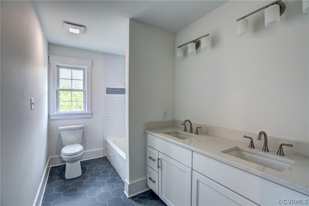 Full bathroom with tile floors, tiled shower / bath, toilet, and dual bowl vanity