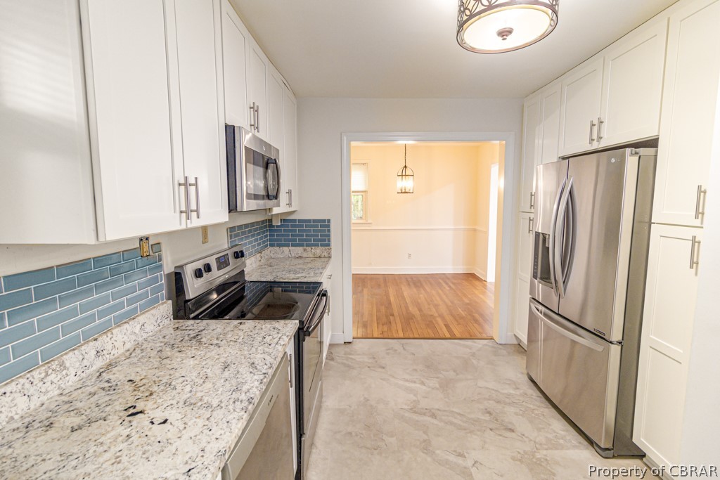 Kitchen featuring white cabinets, tasteful backsplash, light tile floors, and stainless steel appliances