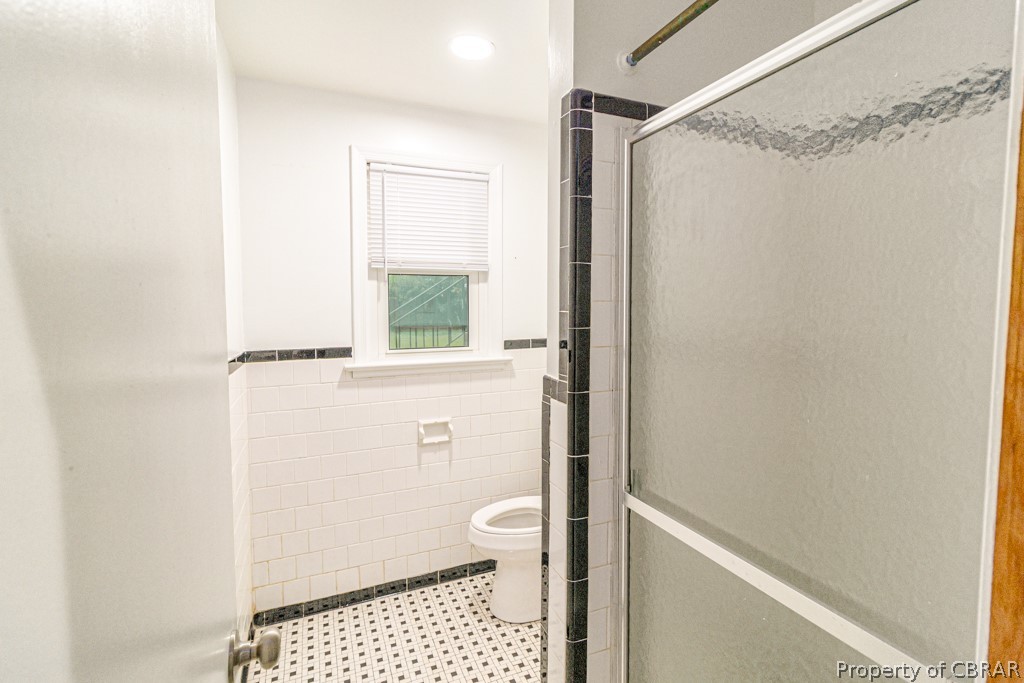 Bathroom with tile walls, tile floors, toilet, and walk in shower