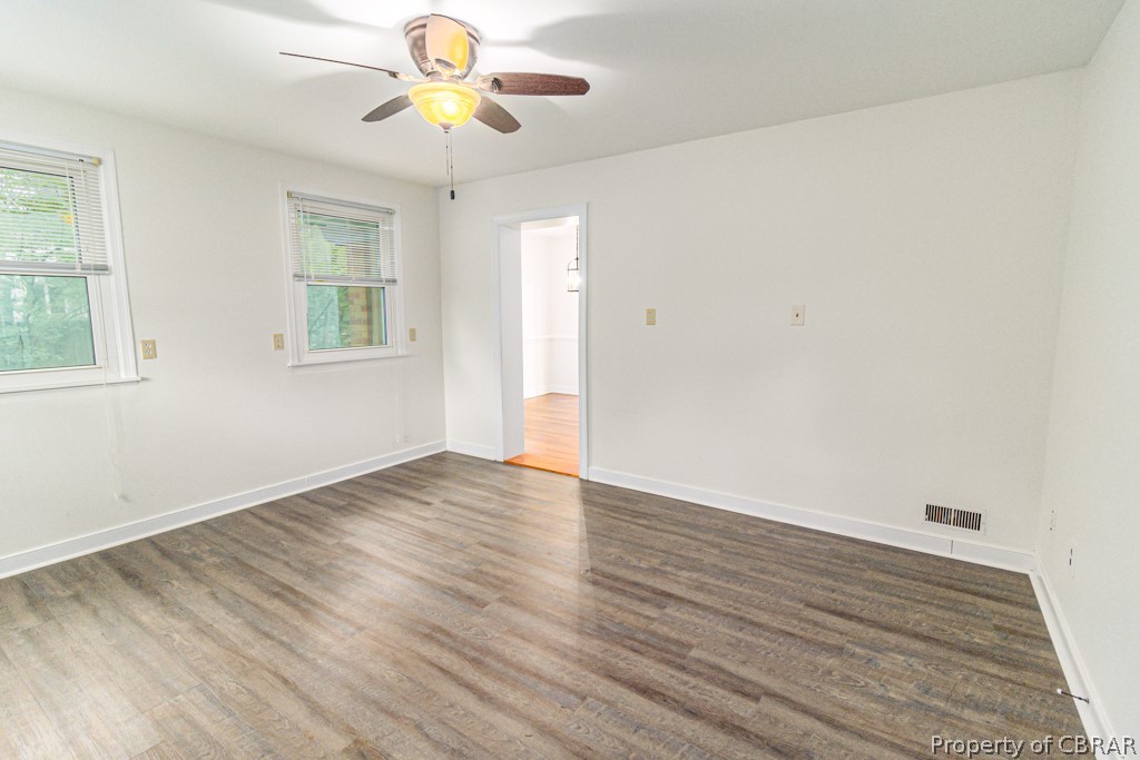 Unfurnished room featuring a healthy amount of sunlight, ceiling fan, and dark wood-type flooring