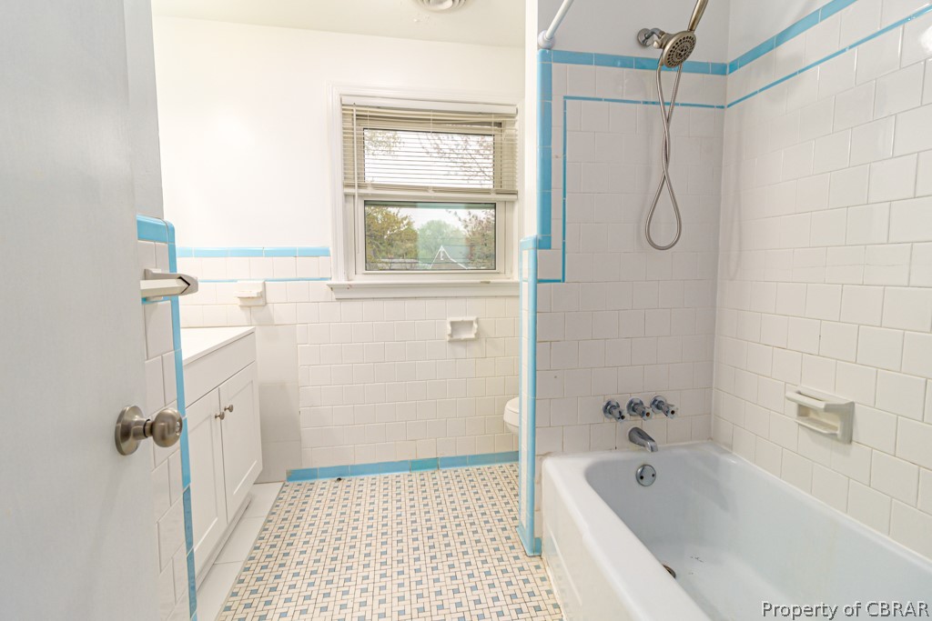 Full bathroom with tile walls, toilet, tiled shower / bath, vanity, and tile floors