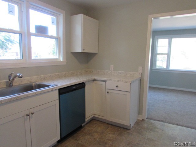 Kitchen with white cabinetry, stainless steel dishwasher, sink, and dark carpet
