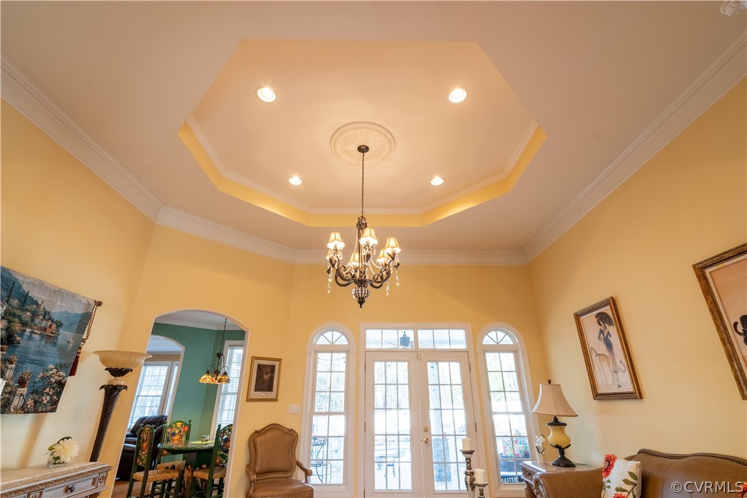 Dining area featuring an inviting Swarovski chandelier, ornate columns, light wood-type flooring, and a tray ceiling