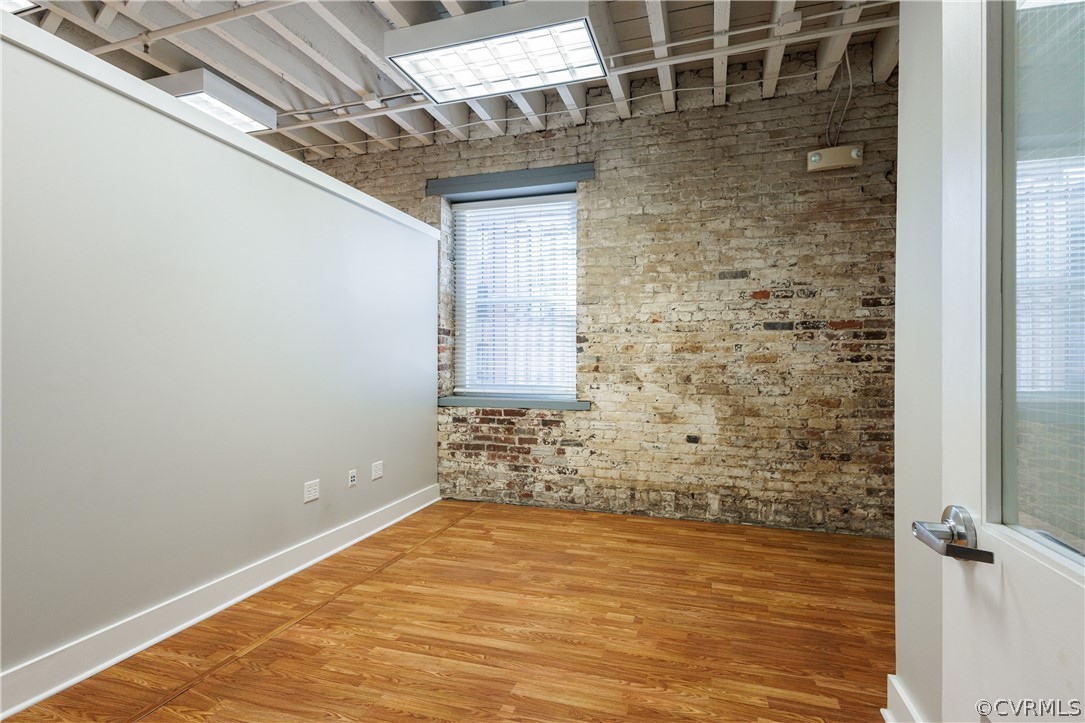 Empty room with light hardwood / wood-style flooring and brick wall