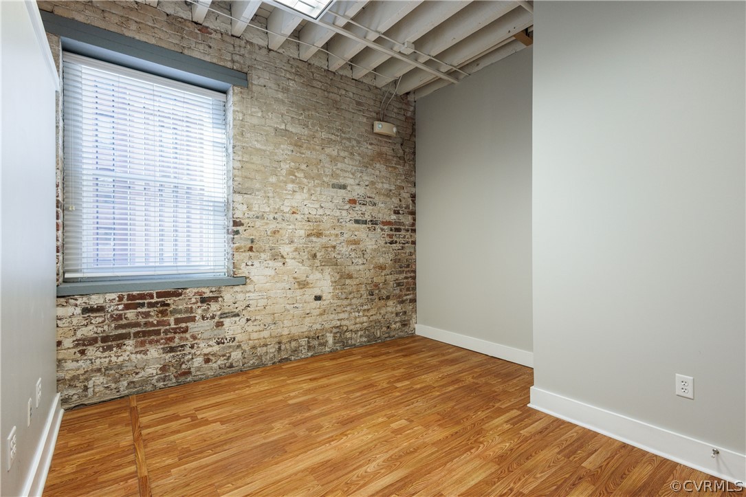 Spare room with light wood-type flooring, brick wall, and plenty of natural light