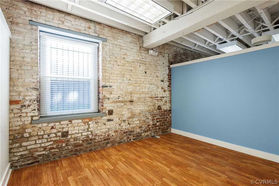 Empty room with brick wall and hardwood / wood-style flooring