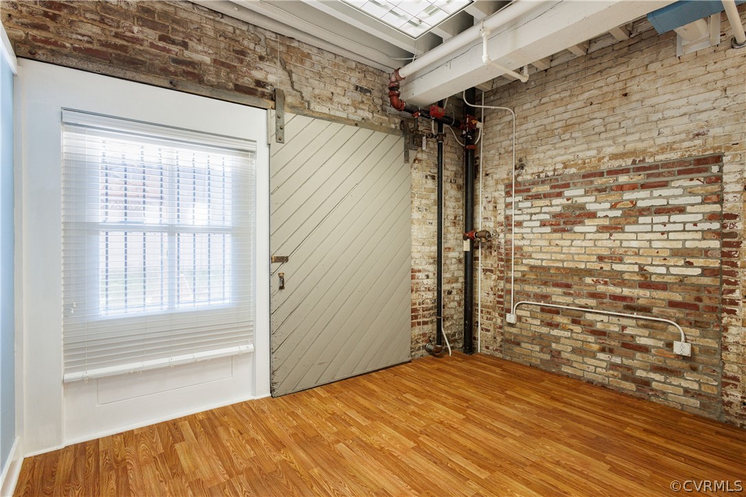 Spare room featuring a barn door, brick wall, and light wood-type flooring