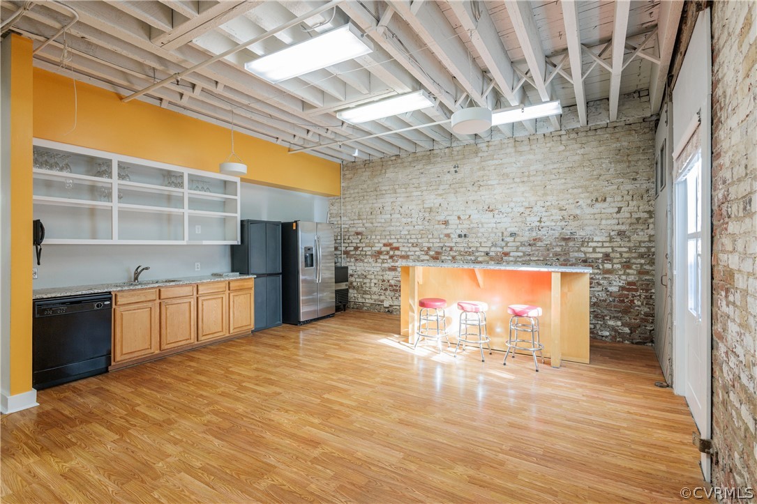 Kitchen featuring light stone counters, light hardwood / wood-style floors, black dishwasher, brick wall, and sink