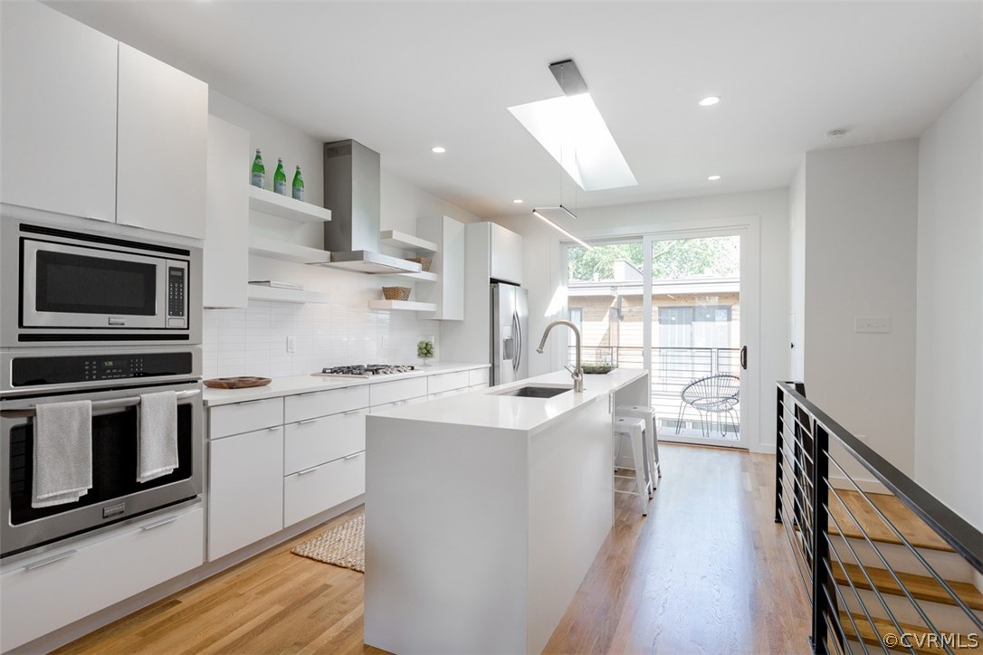 Kitchen featuring sink, stainless steel appliances, white cabinets, and wall chimney range hood