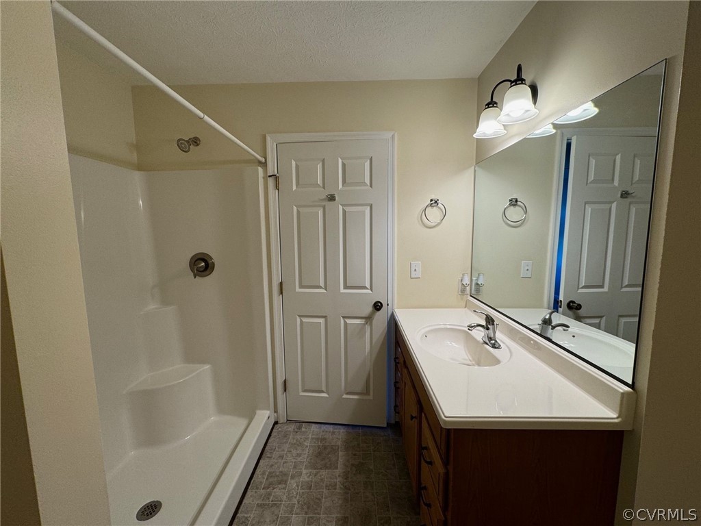 Bathroom with walk in shower, a textured ceiling, and vanity with extensive cabinet space