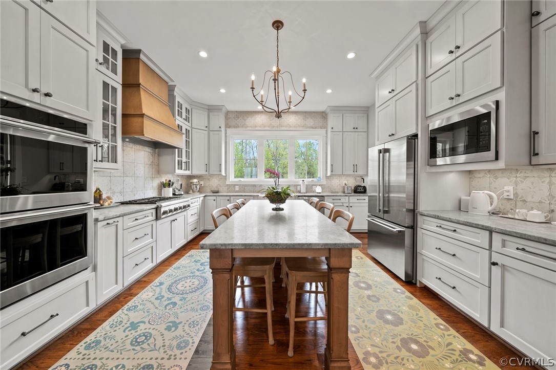 Kitchen with a center island, a breakfast bar, stainless steel appliances, backsplash, and custom exhaust hood