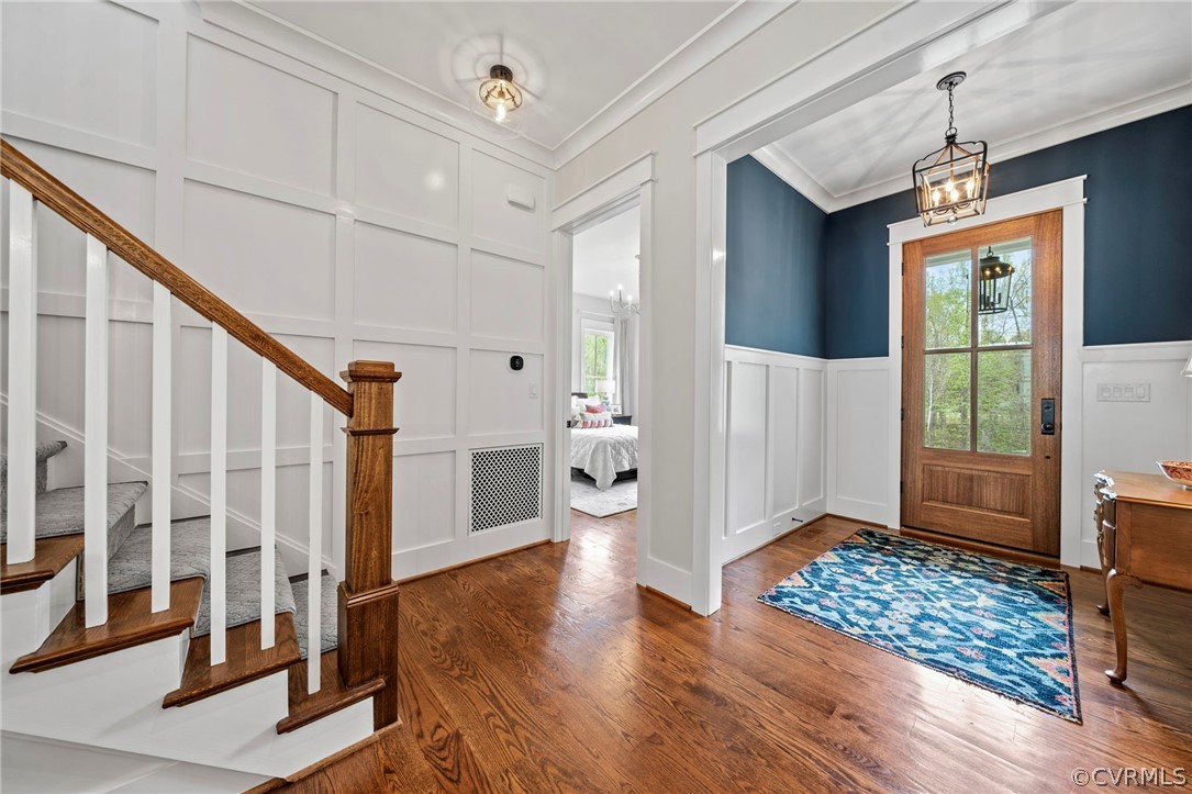 Foyer entrance with crown molding, a notable chandelier, and dark wood-type flooring