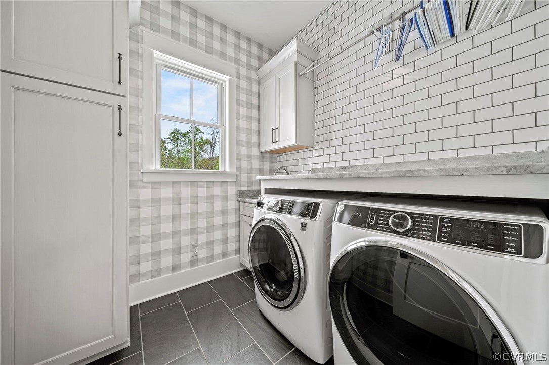 Washroom featuring washer and dryer, cabinets, and dark tile flooring