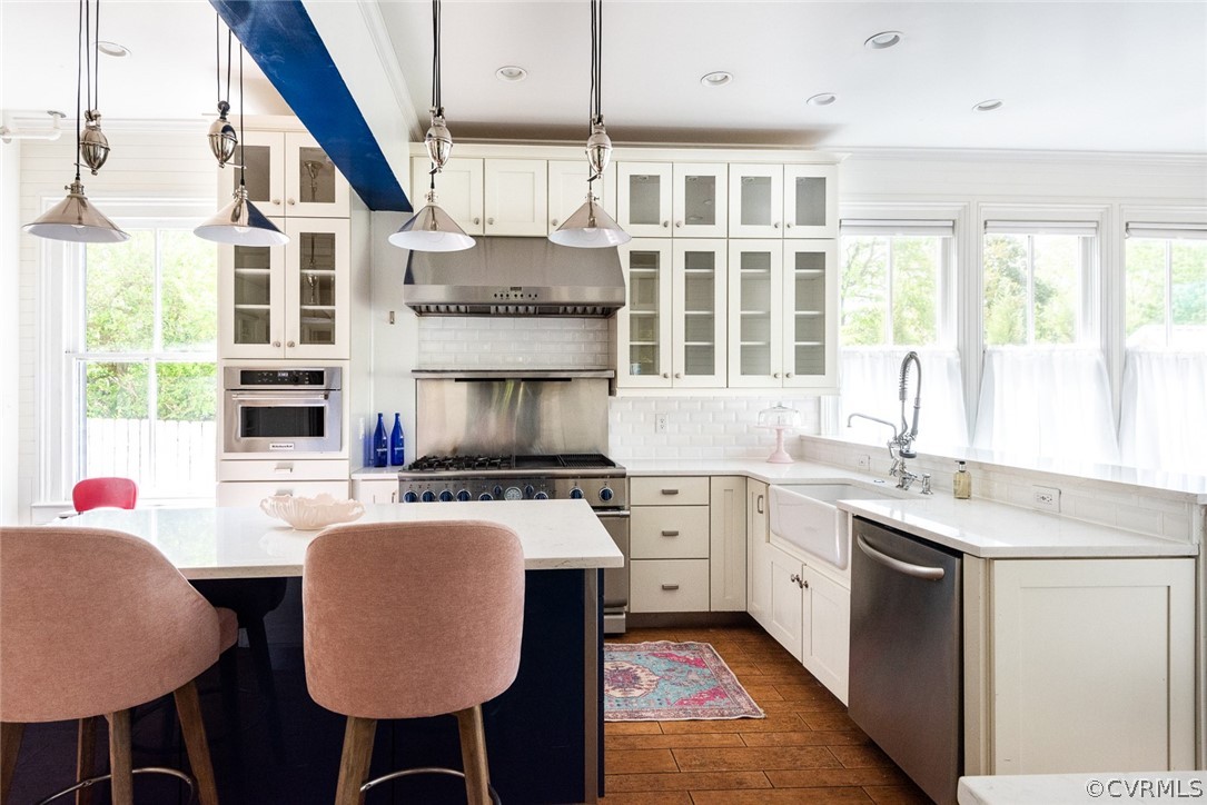 Kitchen featuring backsplash, range hood, appliances with stainless steel finishes, and a healthy amount of sunlight