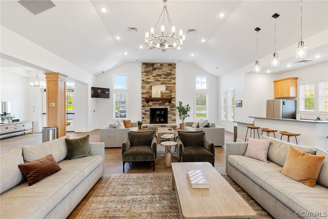 Living room featuring high vaulted ceiling, hardwood / wood-style floors, brick wall, an inviting chandelier, and a stone fireplace