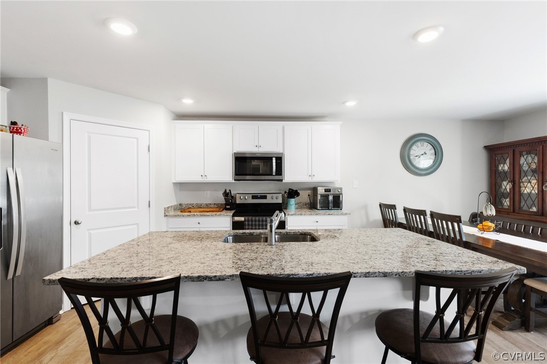 Kitchen featuring appliances with stainless steel finishes, a kitchen island with sink, white cabinets, light wood-type flooring, and a breakfast bar